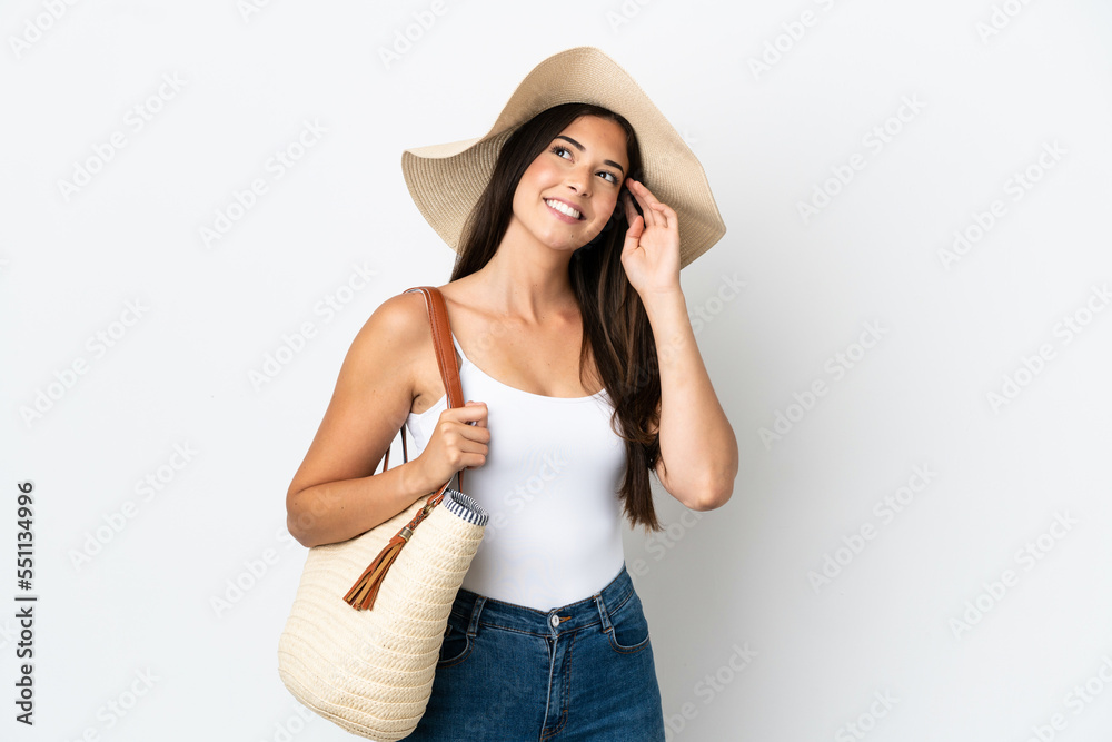 Young Brazilian woman with Pamela holding a beach bag isolated on white background thinking an idea Young Brazilian woman with Pamela holding a beach bag isolated on white background thinking an idea