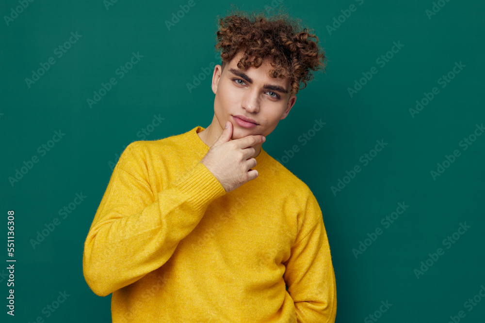 a cute, thoughtful man stands on a green background in a yellow sweater holding his hand to the will of the face. Horizontal photo with empty space a cute, thoughtful man stands on a green background in a yellow sweater holding his hand to the will of the face. Horizontal photo with empty space