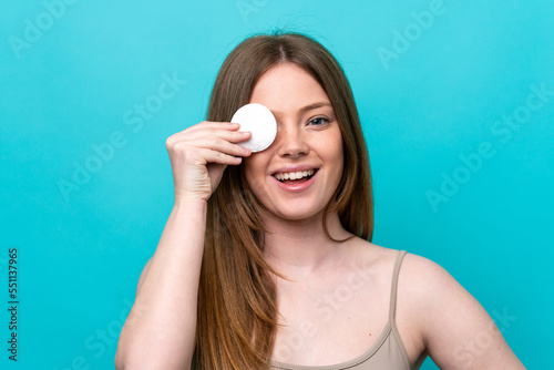 Young caucasian woman isolated on blue background with cotton pad for removing makeup from her face and smiling