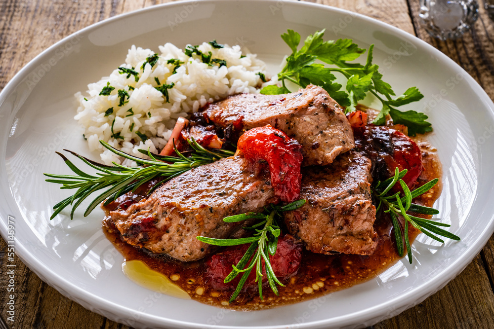 Roast pork loin with plums in sauce and white rice on wooden table
