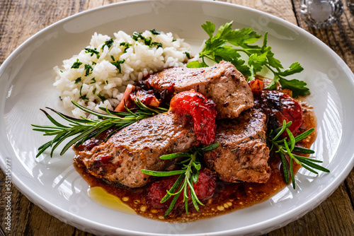 Roast pork loin with plums in sauce and white rice on wooden table 