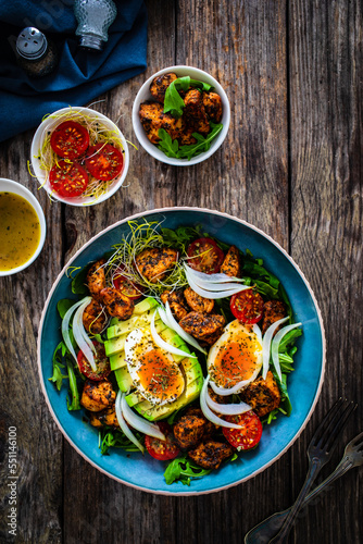 Tasty salad - fried chicken breast  avocado  boiled eggs  mini tomatoes and fresh green vegetables on wooden background 