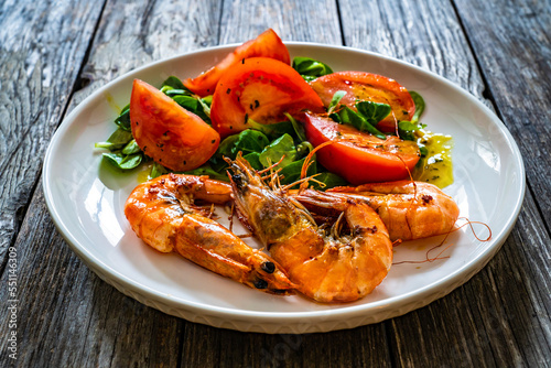 Fried prawns in garlic sauce with greens and tomatoes on wooden table