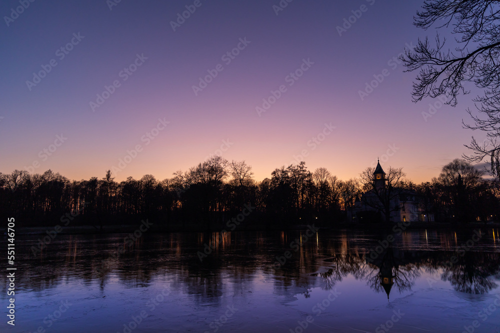 Colorful dramatic sky during sunset over the trees in the palace park. Dark outlines of trees on the near horizon. Contours of the palace in the distance Colorful dramatic sky during sunset over the trees in the palace park. Dark outlines of trees on the near horizon. Contours of the palace in the distance