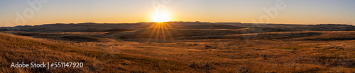 Long panorama of a sunset over a golden autumn prairie. The small hills are highlighted by the late day sun. The sun appears as a sunstar. 