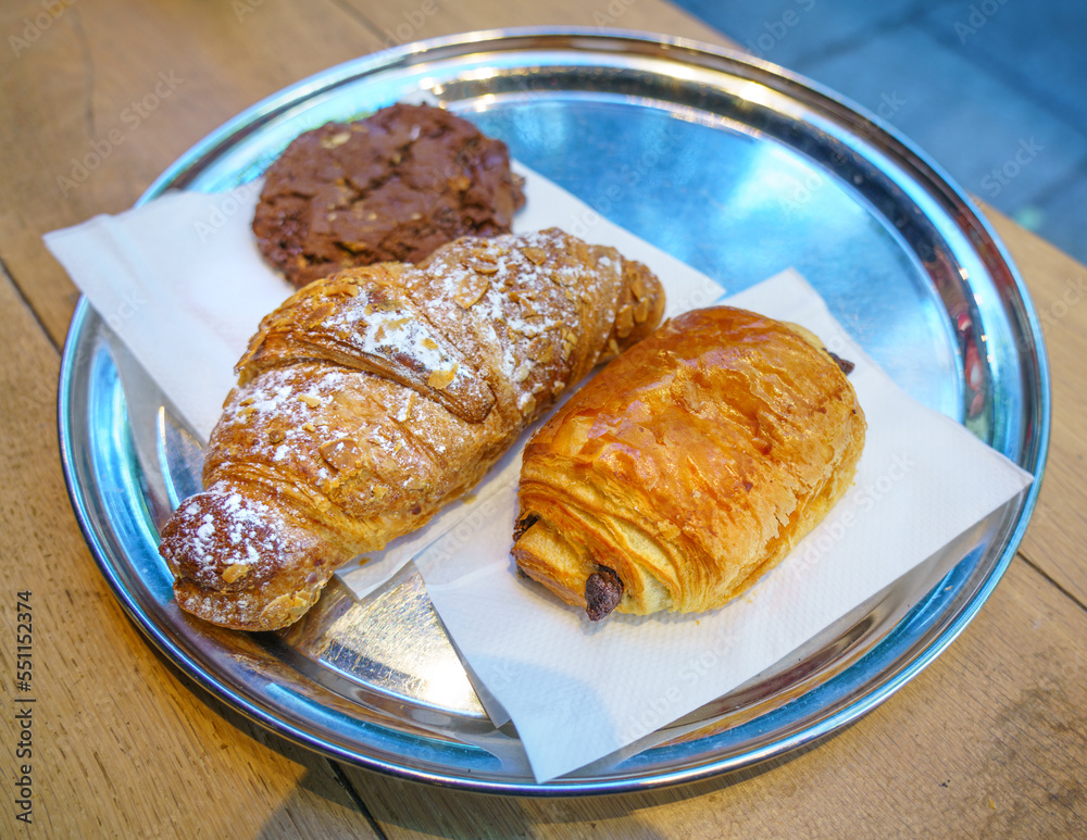 Delicious French breakfast on metal plate consist of fresh Pain au chocolate, croissant and chocolate cookie. Selective focus on Pain au chocolate crust 
