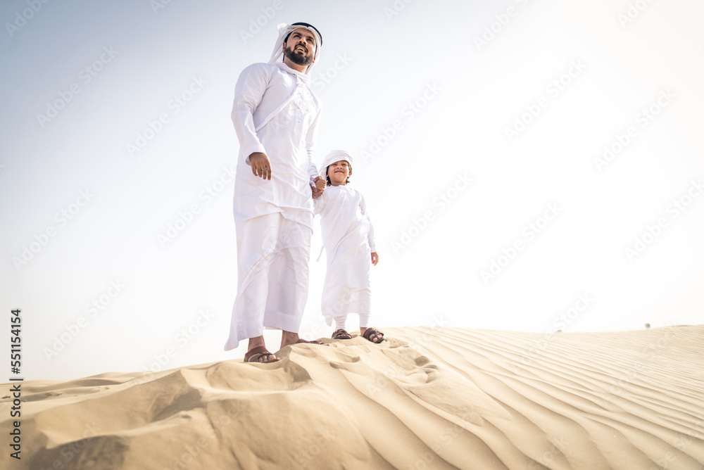 Arabian man and son wearing traditional emirates kandora dress playing in the desert