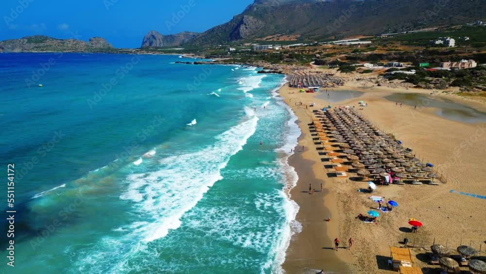 Aerial view of a Greek Island's sandy beach, turquoise water, umbrellas, and azure sea with white waves Aerial view of a Greek Island's sandy beach, turquoise water, umbrellas, and azure sea with white waves