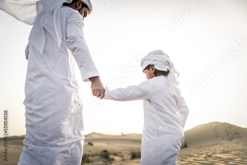 Playful arab man and his son wering traditional middle eastern emirate clothing playing and having fun in the desert of Dubai