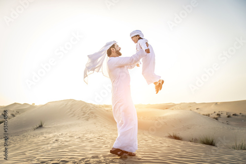Playful arab man and his son wering traditional middle eastern emirate clothing playing and having fun in the desert of Dubai