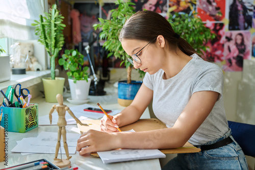 Teenage girl drawing sketches with pencil, sitting at table at home