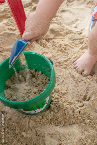 child digging hole in clean beach sand during sunny day with family, using shovel and plastic bucket, playing and having fun