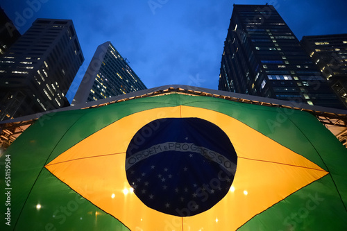 Brazilian flag at street with high buildings at night. Brazil's national symbol backlit. Patriotic growth concept. 