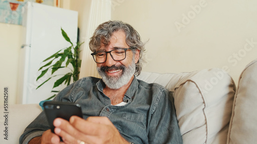 Middle-aged man relaxing on his couch while in home and using his smartphone to text