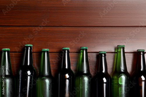 Glass bottles of beer on wooden background, flat lay. Space for text