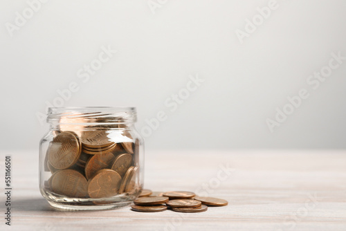 Glass jar with coins on white wooden table. Space for text