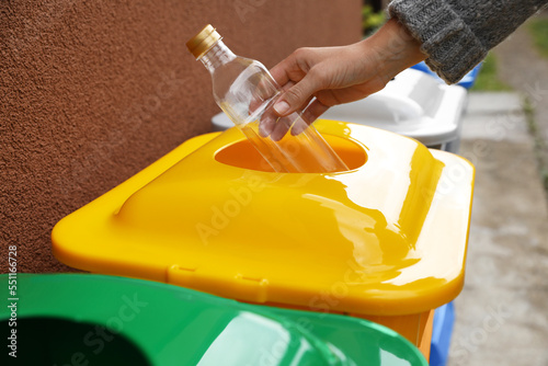 Woman throwing bottle into recycling bin outdoors, closeup