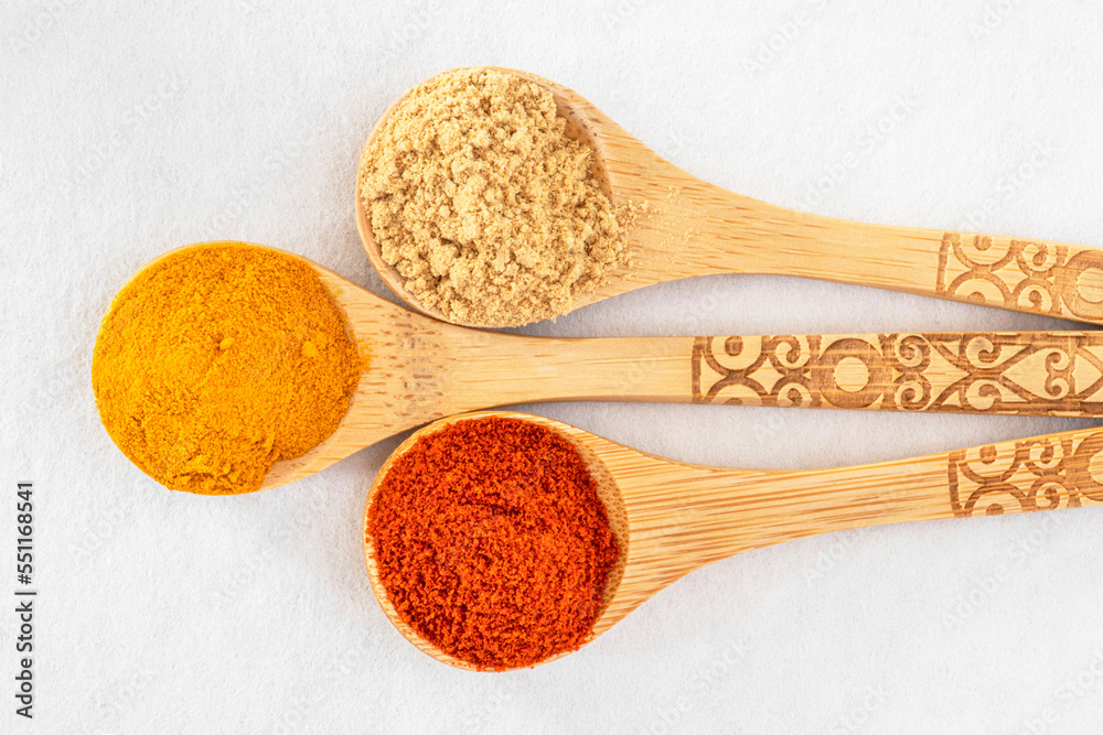 Close-up of coloured spices in wooden spoons on a white background Close-up of coloured spices in wooden spoons on a white background