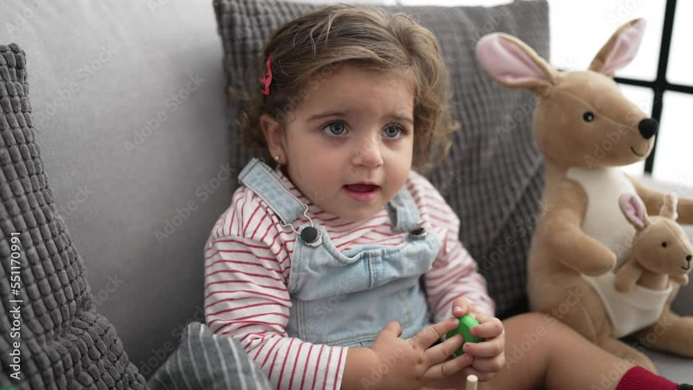 Adorable hispanic girl playing with hoops game sitting on sofa by christmas tree at home