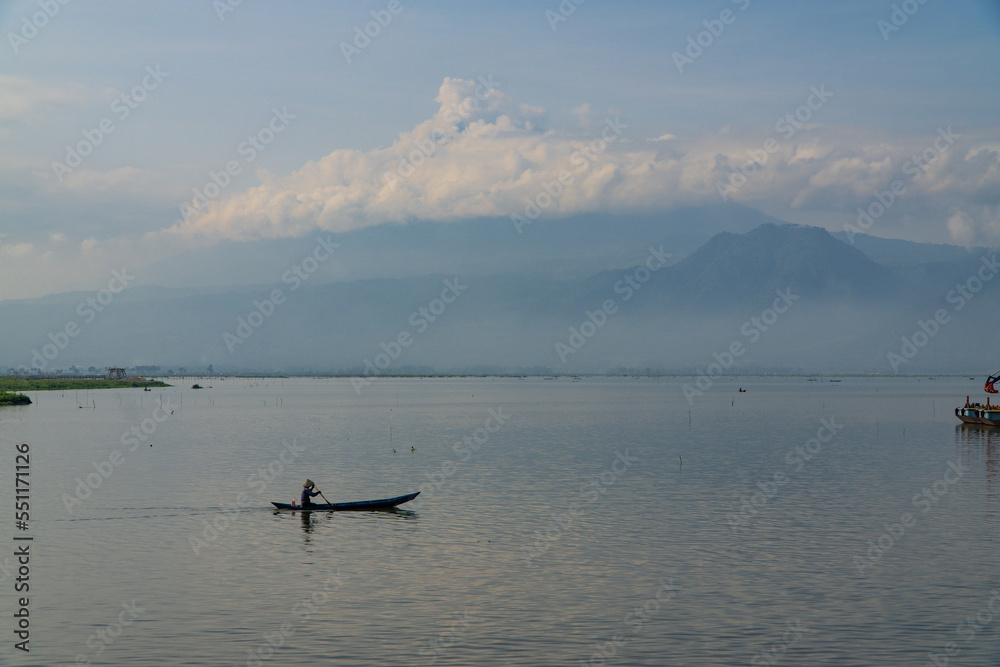 Traditional fishing boat looking for fish in the lake with mountains and hills in the background - Rawa Pening Lake, Semarang, Indonesia