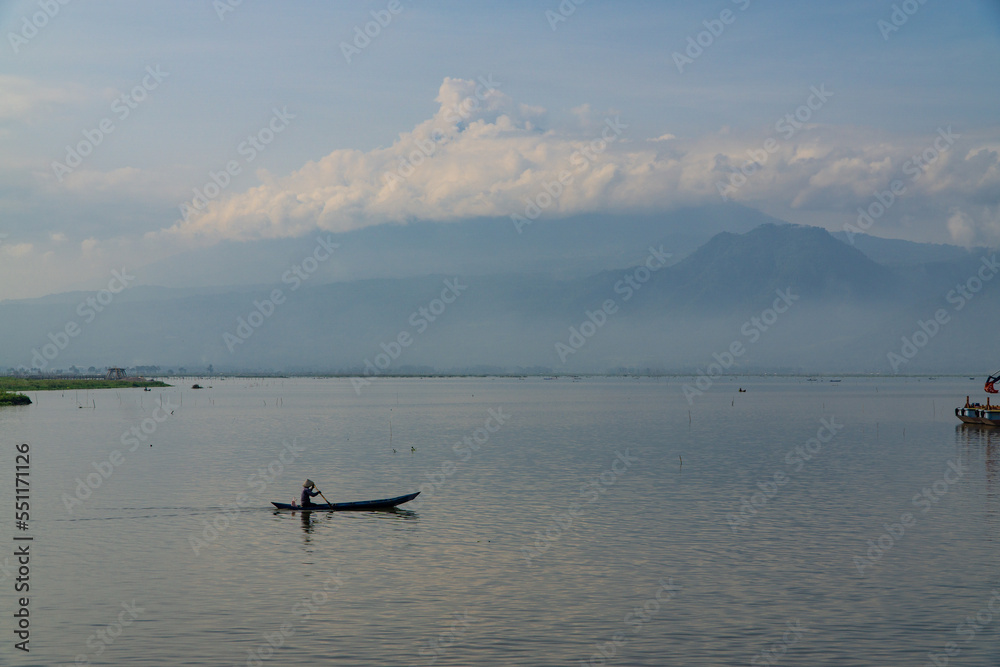 Obraz premium Traditional fishing boat looking for fish in the lake with mountains and hills in the background - Rawa Pening Lake, Semarang, Indonesia