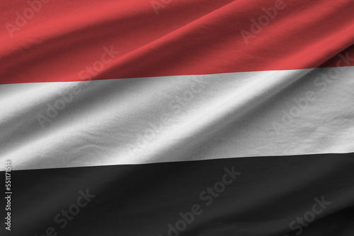 Yemen flag with big folds waving close up under the studio light indoors. The official symbols and colors in fabric banner photo