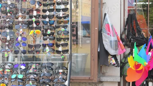 HUSTOPECE, CZECHIA - NOVEMBER 26, 2022: Display rack with sunglasses in front of a small general shop. Retail rack with various sunglasses in front of a variety store. The boxes with artificial photo