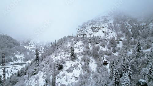 Cable car in the mountains in the winter forest. The cabins move along the gondola road through the winter snow forest and fog. White clouds covered the mountains. Top view from a drone. Medeo, Almaty © SergeyPanikhin