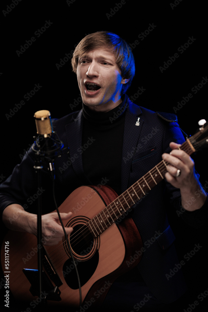 Obraz premium Male musician with guitar in hands playing and posing on black background in blue scenic light