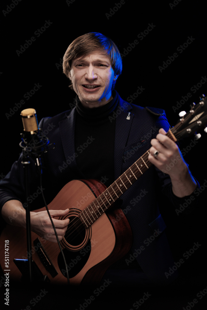 Fototapeta premium Male musician with guitar in hands playing and posing on black background in blue scenic light
