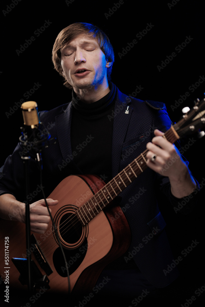 Male musician with guitar in hands playing and posing on black background in blue scenic light Male musician with guitar in hands playing and posing on black background in blue scenic light
