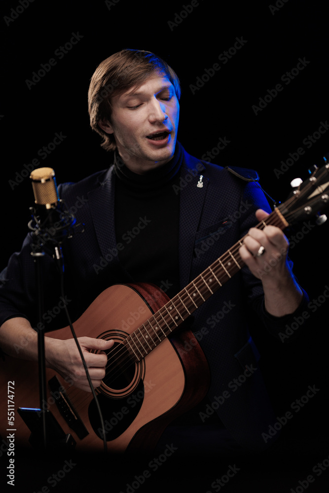 Obraz premium Male musician with guitar in hands playing and posing on black background in blue scenic light