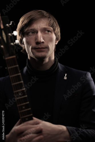 Male musician with guitar in hands playing and posing on black background in blue scenic light