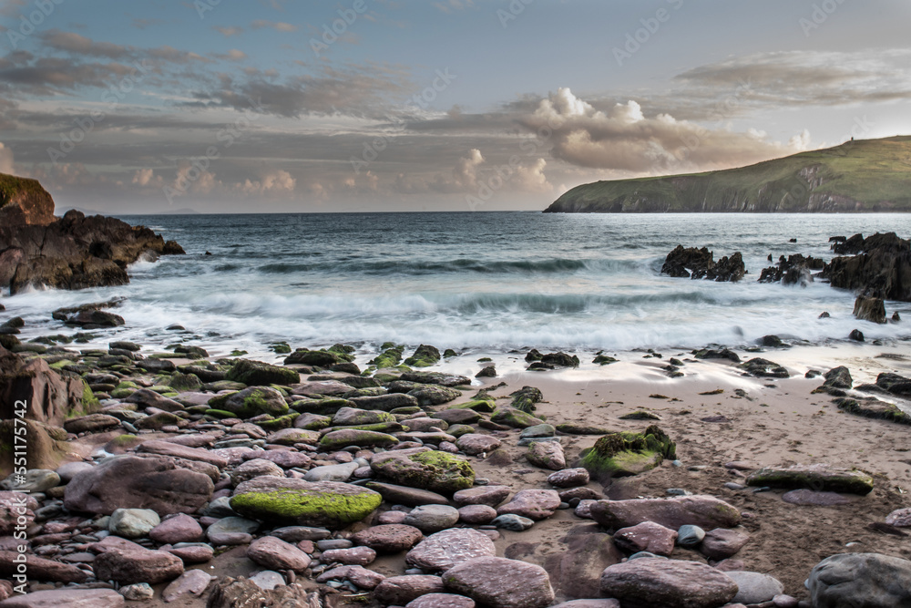 A bay with a sandy beach with a dark clouded sky and green grass and cliffs and a sandy beach at Beenbane, Ireland