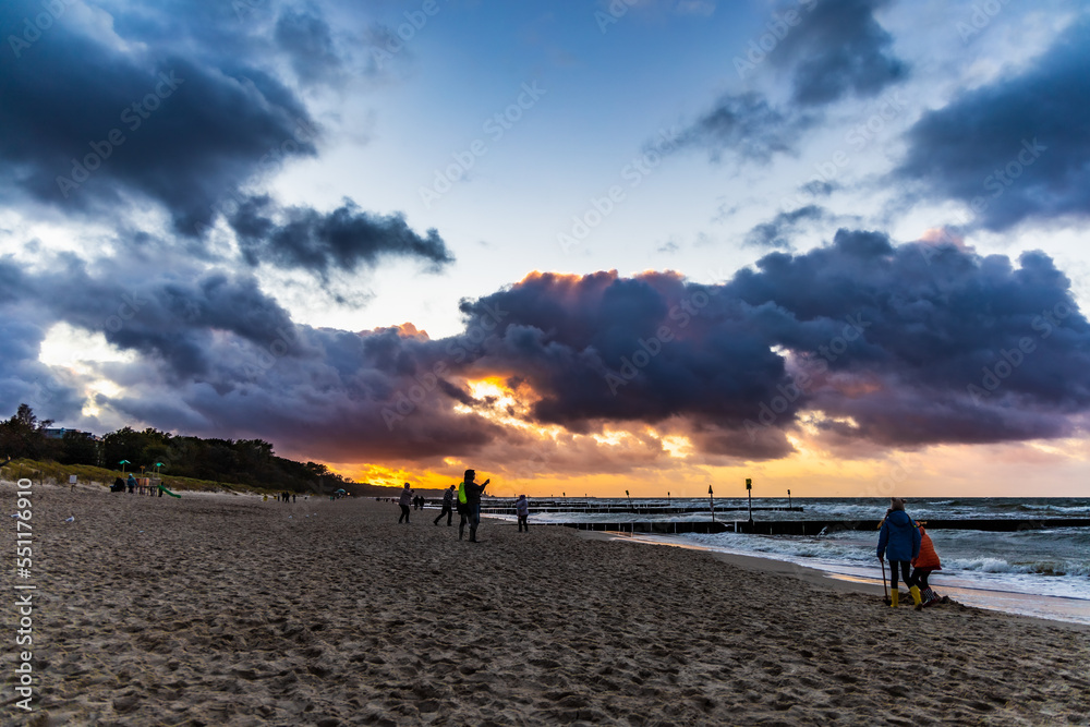 People walking on sandy beach at dark cloudy sunset next to Baltic sea coast