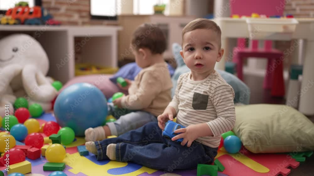 Two adorable toddlers playing with balls and car sitting on floor at kindergarten