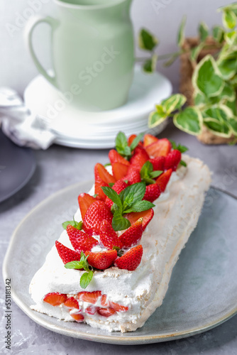 Meringue roll with strawberries and curd cream. Dessert decorated with berries and mint leaves. Homemade baking.