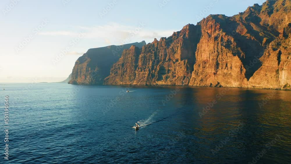 Orange sunset light illuminate majestic rocky barren volcanic mountains Los Gigantes with dark deep ocean water, beachfront. Aerial flight over sea, cliffs silhouette. Nature seascape. Tenerife. Orange sunset light illuminate majestic rocky barren volcanic mountains Los Gigantes with dark deep ocean water, beachfront. Aerial flight over sea, cliffs silhouette. Nature seascape. Tenerife.