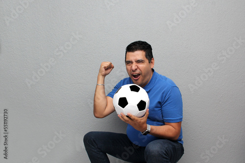 Latino adult man plays with a soccer ball very excited that he is going to see a game and wants to see his team win