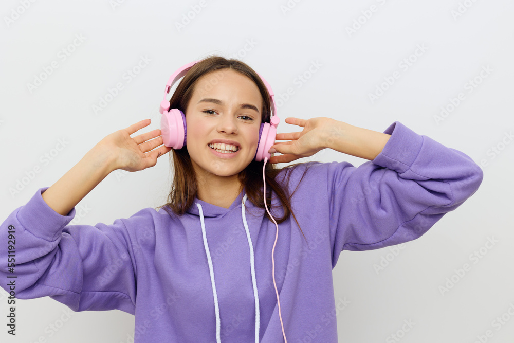 horizontal studio photo of a happy, joyful woman in a purple tracksuit listening to music holding her pink headphones with both hands and smiling broadly looking at the camera horizontal studio photo of a happy, joyful woman in a purple tracksuit listening to music holding her pink headphones with both hands and smiling broadly looking at the camera