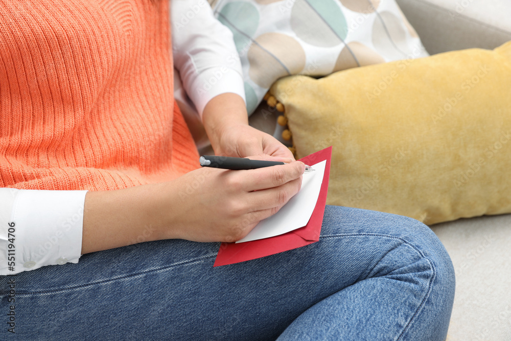 Young woman writing message in greeting card on sofa, closeup