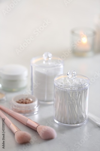 Cotton buds and pads in transparent holders near makeup brushes on table indoors