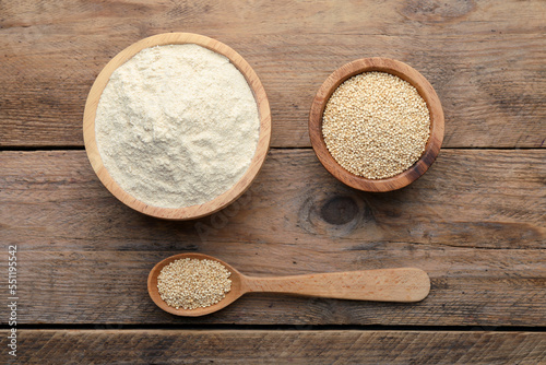 Quinoa flour in bowls and spoon with seeds on wooden table, flat lay