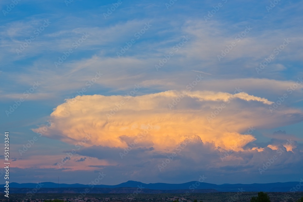 Huge white and orange cloud, with smaller white clouds, at sunset over the mountains near Sedona, Arizona