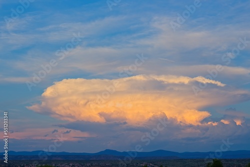 Huge white and orange cloud, with smaller white clouds, at sunset over the mountains near Sedona, Arizona