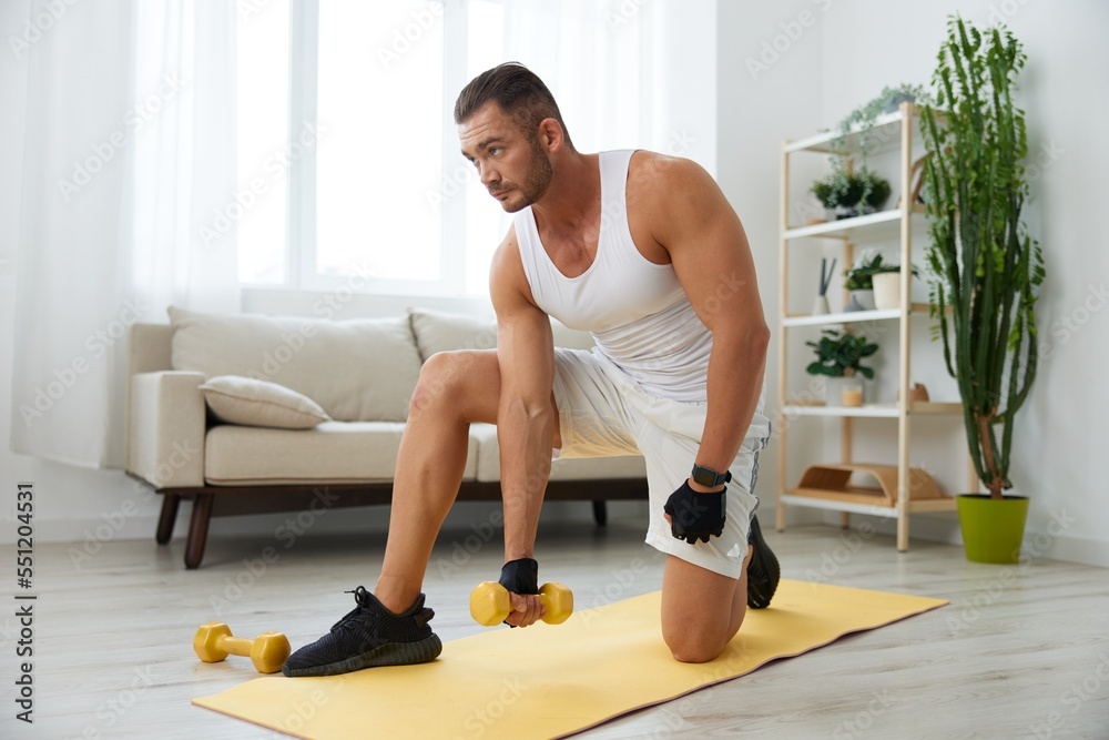 Man sports home training on the floor on a mat with dumbbells, exercises for muscle growth, pumped up man fitness trainer exercises at home, the concept of health and beauty of the body Man sports home training on the floor on a mat with dumbbells, exercises for muscle growth, pumped up man fitness trainer exercises at home, the concept of health and beauty of the body