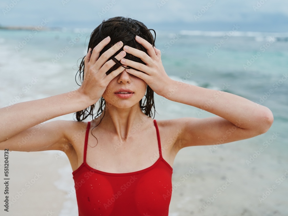 Sexy woman in red swimsuit on ocean beach with wet hair covers face ...