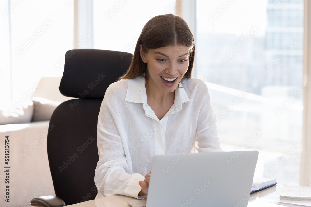 Happy excited young office worker woman getting good news, online message, email, notice, celebrating success, achieve, luck, staring at laptop display, gasping, smiling, laughing Happy excited young office worker woman getting good news, online message, email, notice, celebrating success, achieve, luck, staring at laptop display, gasping, smiling, laughing