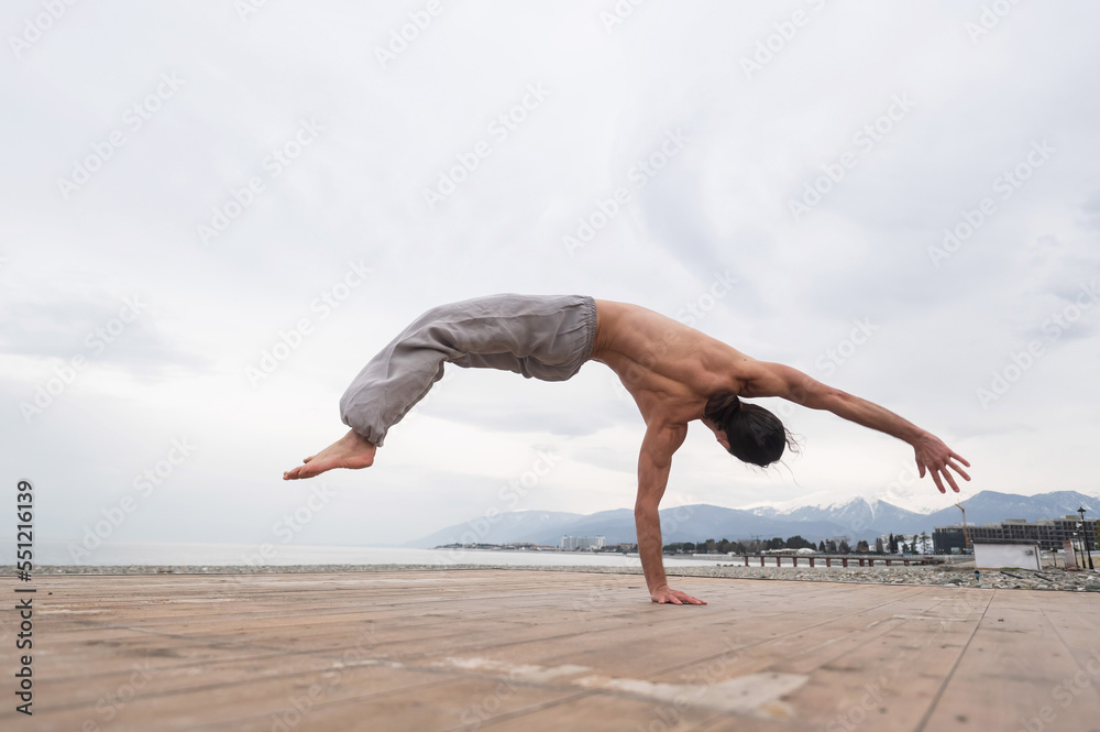 Fototapeta premium Shirtless caucasian man doing backflip on pebble beach. 