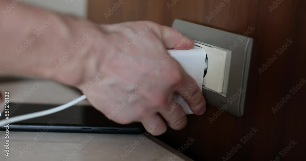 Hand inserts plug into electrical outlet charges phone from usb device Hand inserts plug into electrical outlet charges phone from usb device
